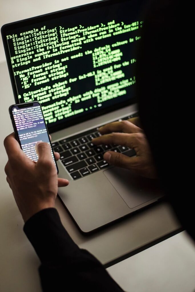 Person using a smartphone and laptop with code on the screen